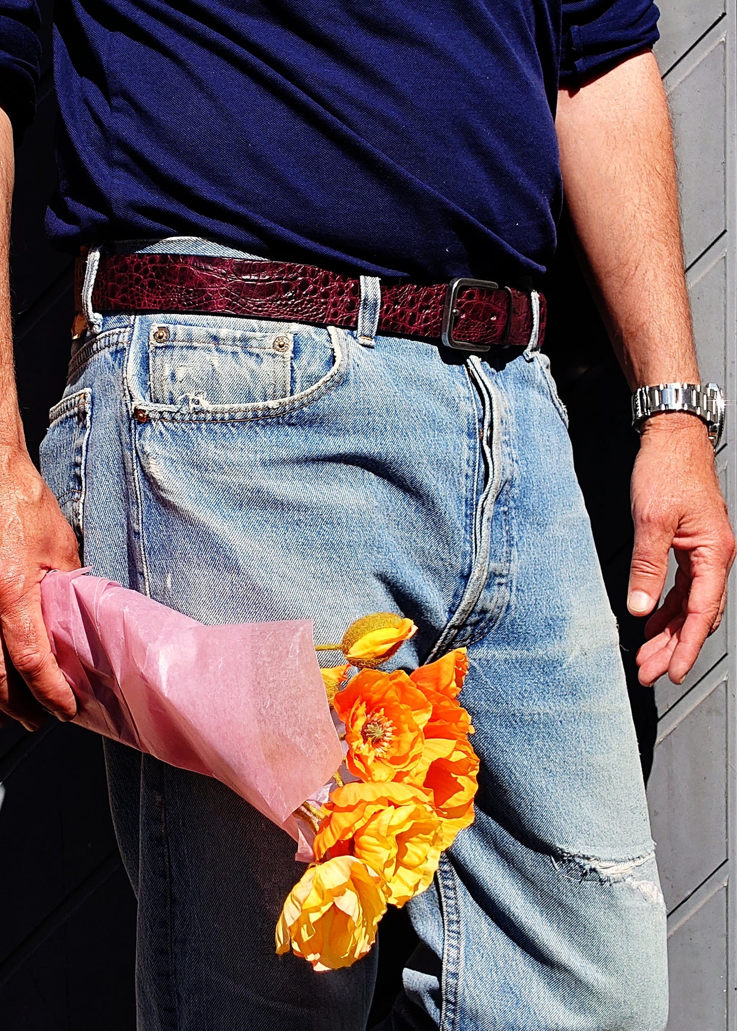Lifestyle shot of the Dirty Aubergine belt worn with blue jeans, held by a person carrying orange flowers.