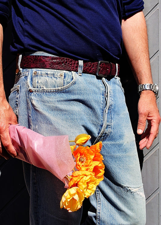 Lifestyle shot of the Dirty Aubergine belt worn with blue jeans, held by a person carrying orange flowers.