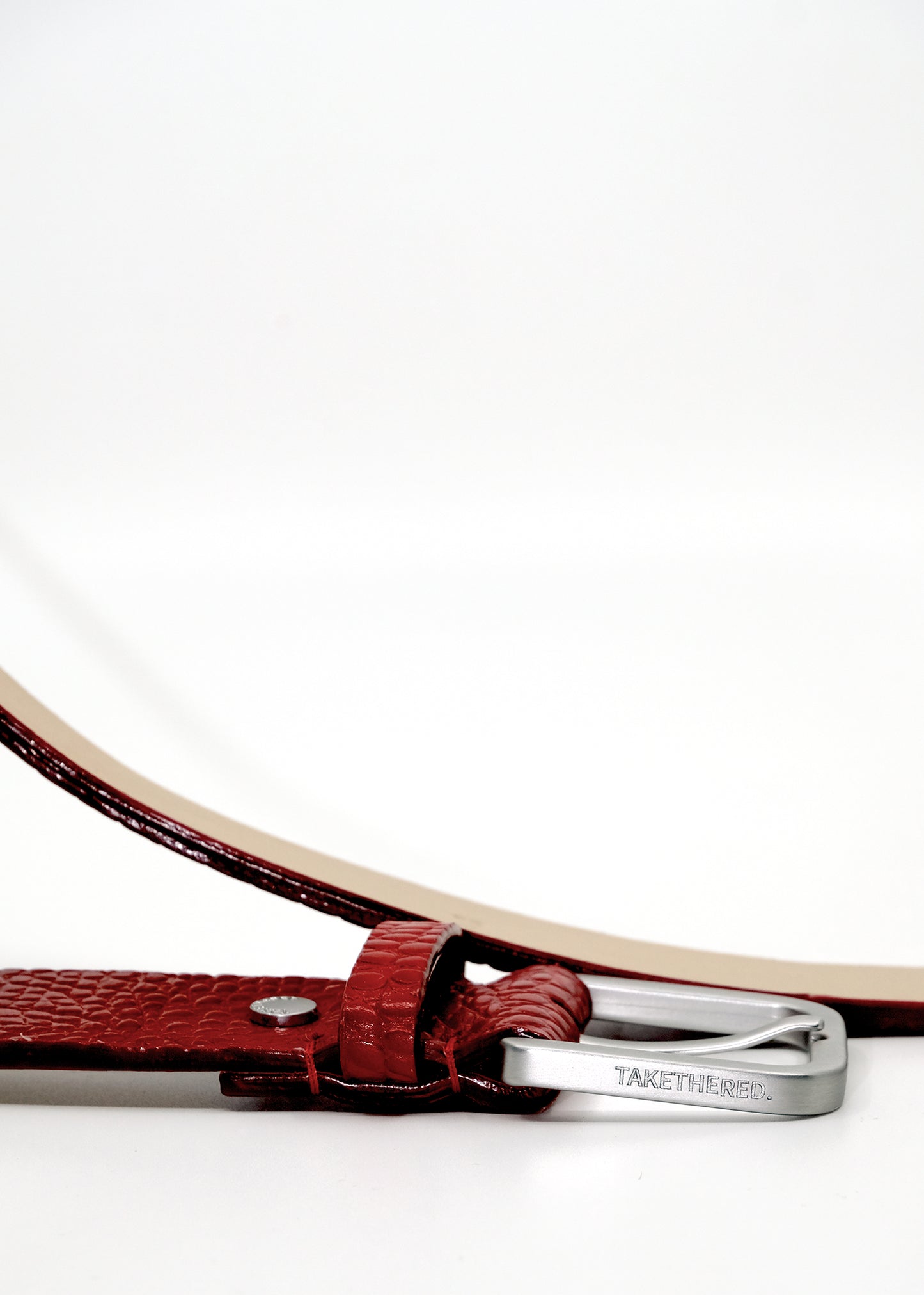 Side view of the Blood red Mississippi Belt buckle in silver metal, engraved with the "TAKETHERED" brand name.