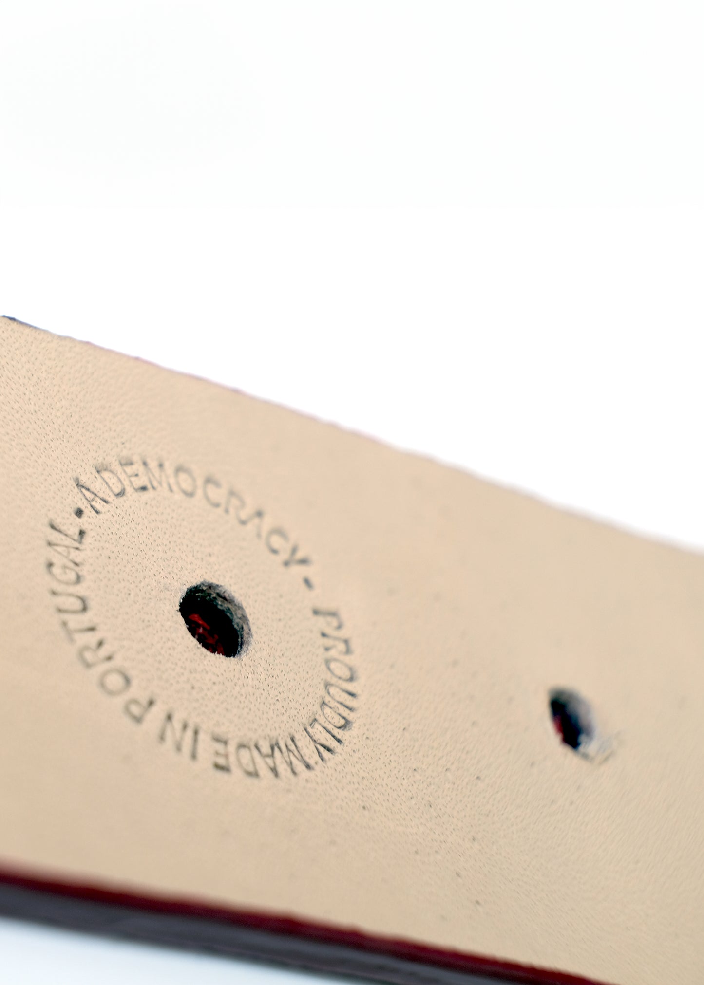 Interior view of the blood red belt showing the silver metal buckle and a "PROUDLY MADE IN PORTUGAL" stamp.