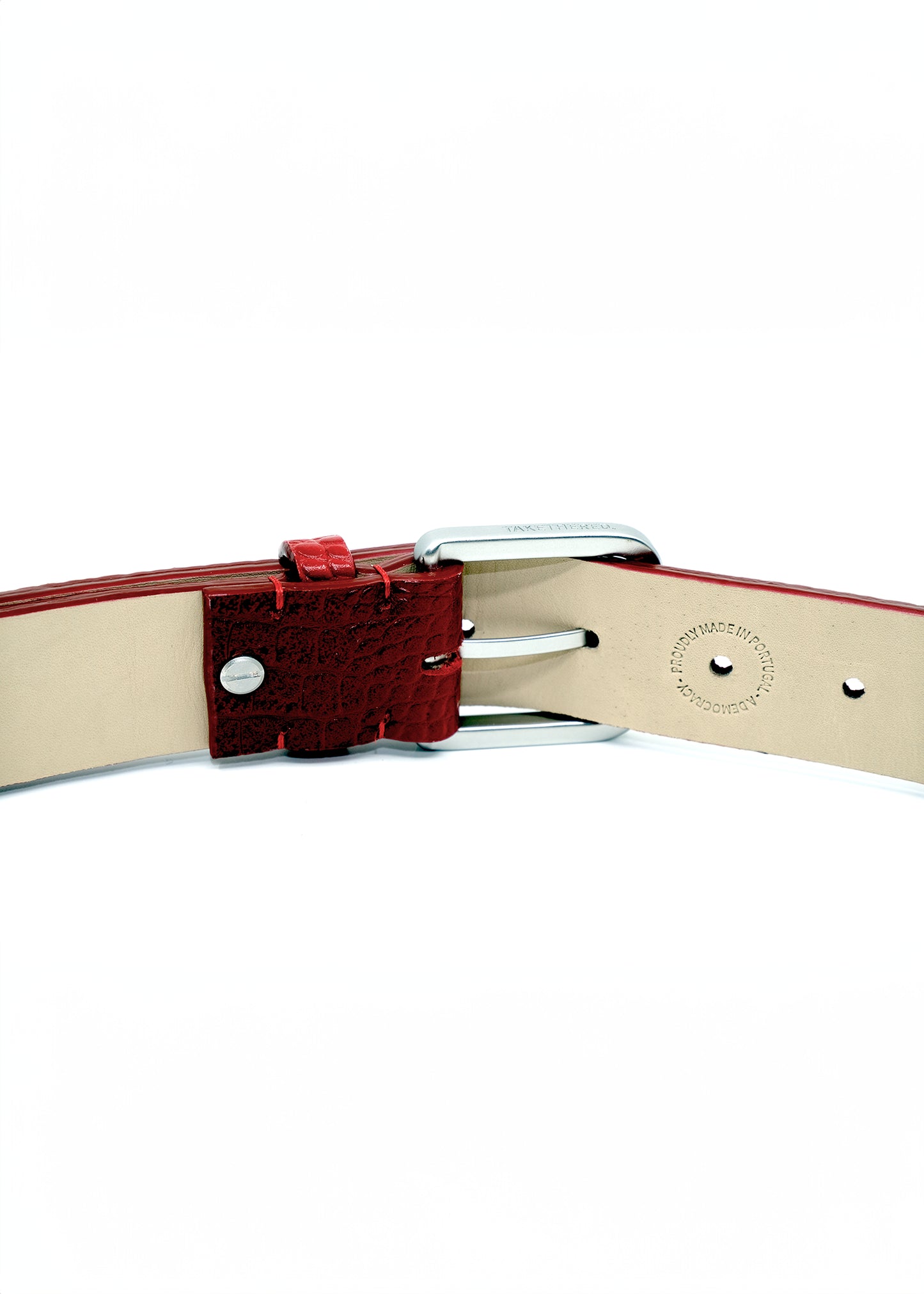 Interior view of a blood red belt showing a silver metal buckle and a "PROUDLY MADE IN PORTUGAL" embossed stamp.