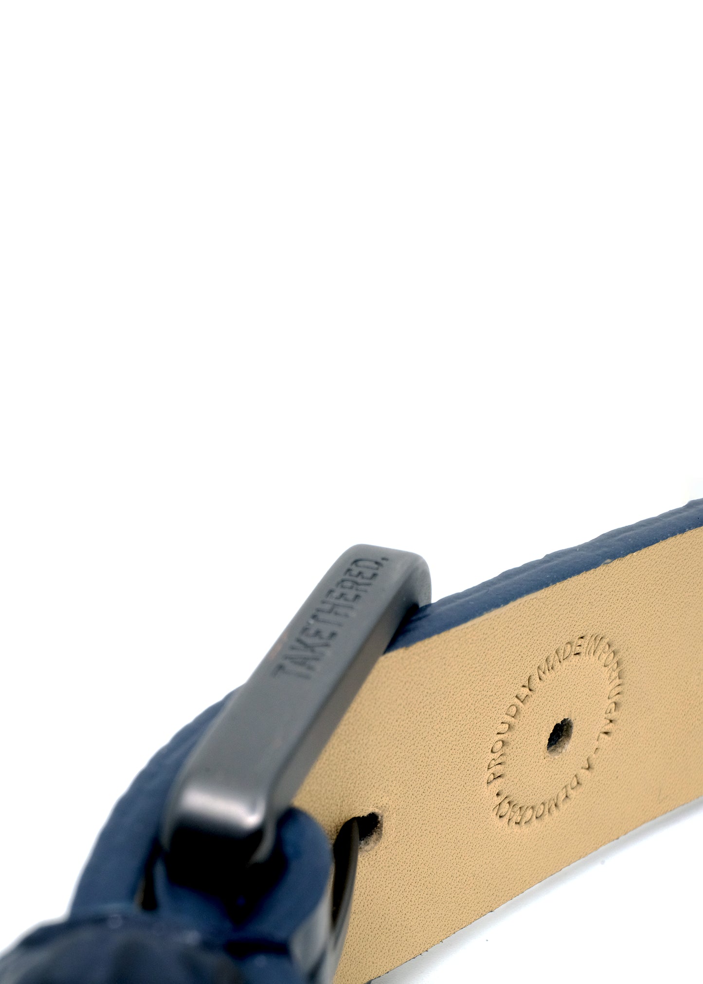 Interior view of a navy belt showing a matte black buckle and a "PROUDLY MADE IN PORTUGAL" embossed stamp.