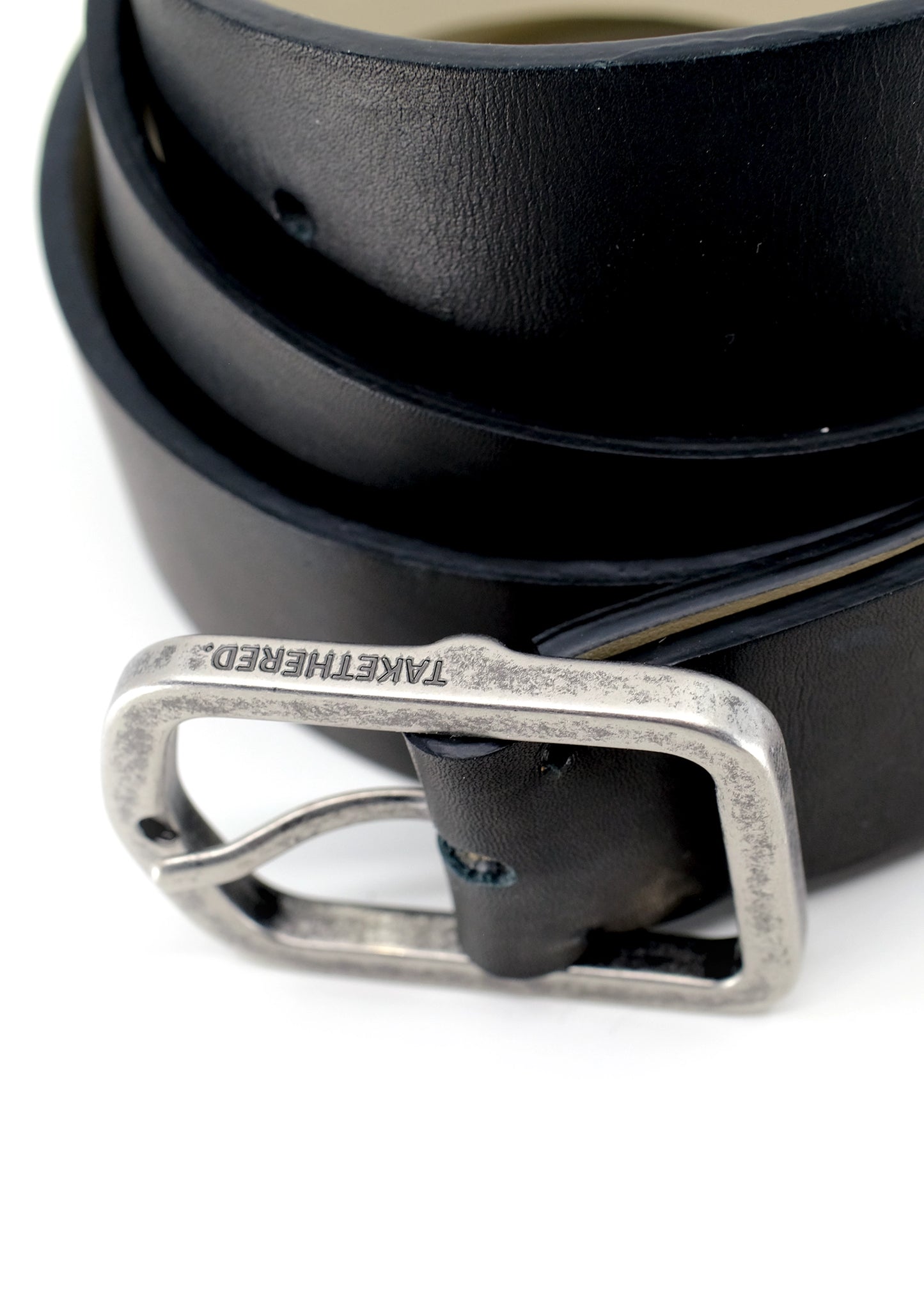 Macro shot of a Classic Pitch Black leather belt with a weathered silver buckle featuring an engraved logo.