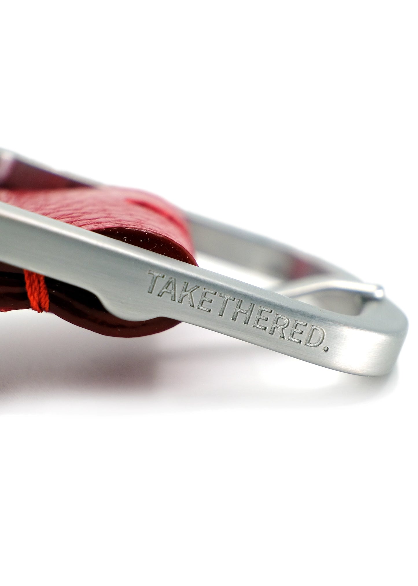 Side view close-up of a weathered silver buckle engraved with "TAKETHERED." on a red Blood Simple Grunge Belt.