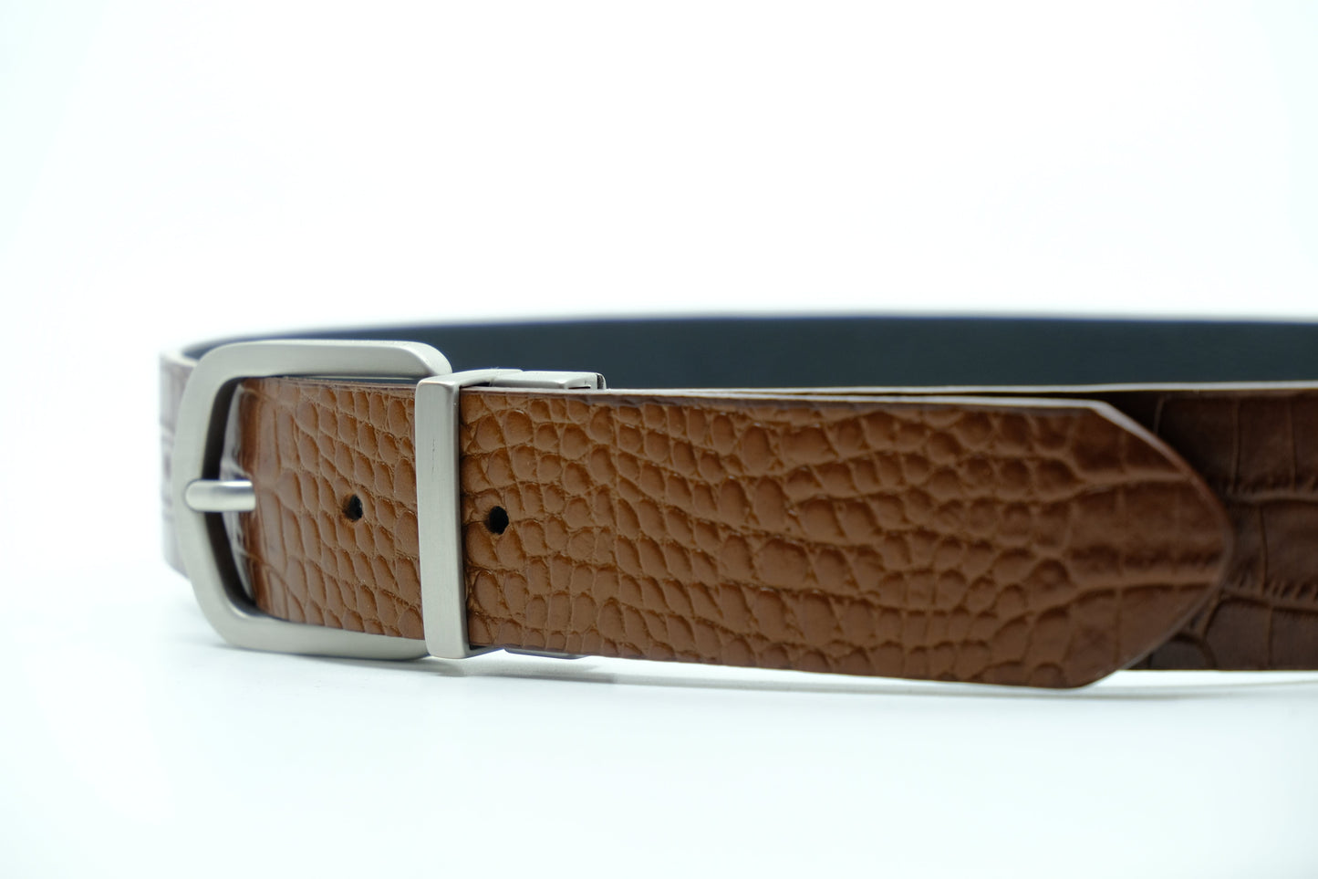 Close-up of Two-Face Belt in Smokey Cognac crocodile leather with a reversible silver buckle and visible black reverse.