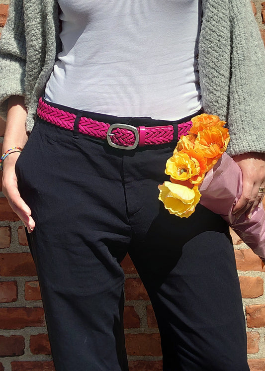 Lifestyle shot of the Barbie Pink braided belt worn with black trousers, paired with a white top and orange flowers.