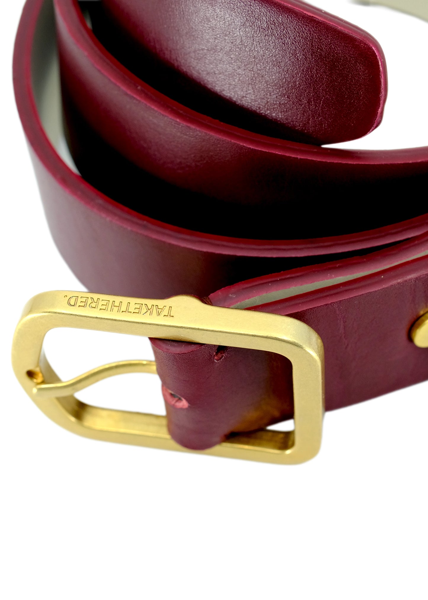 Close-up of Classic Red Mist burgundy leather belt with a matte gold buckle and engraved "TAKETHERED." logo.