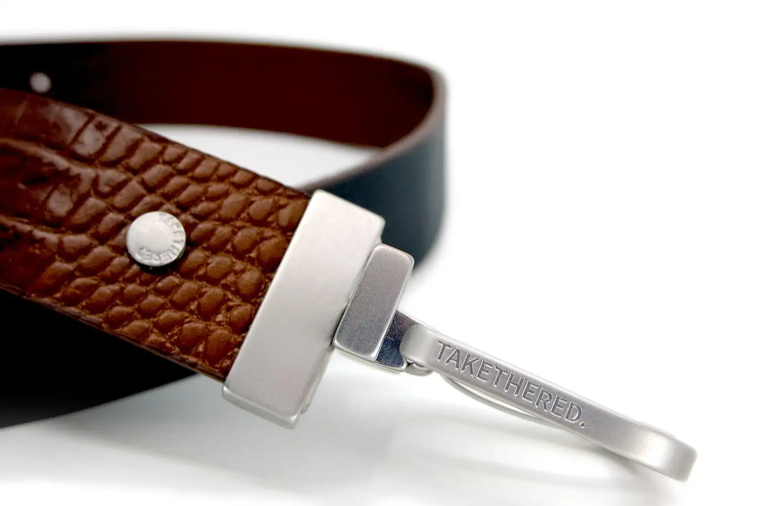 An extreme close-up of a Two-Face turnable leather belt in chocolate brown and black with a logo embossed silver buckle.