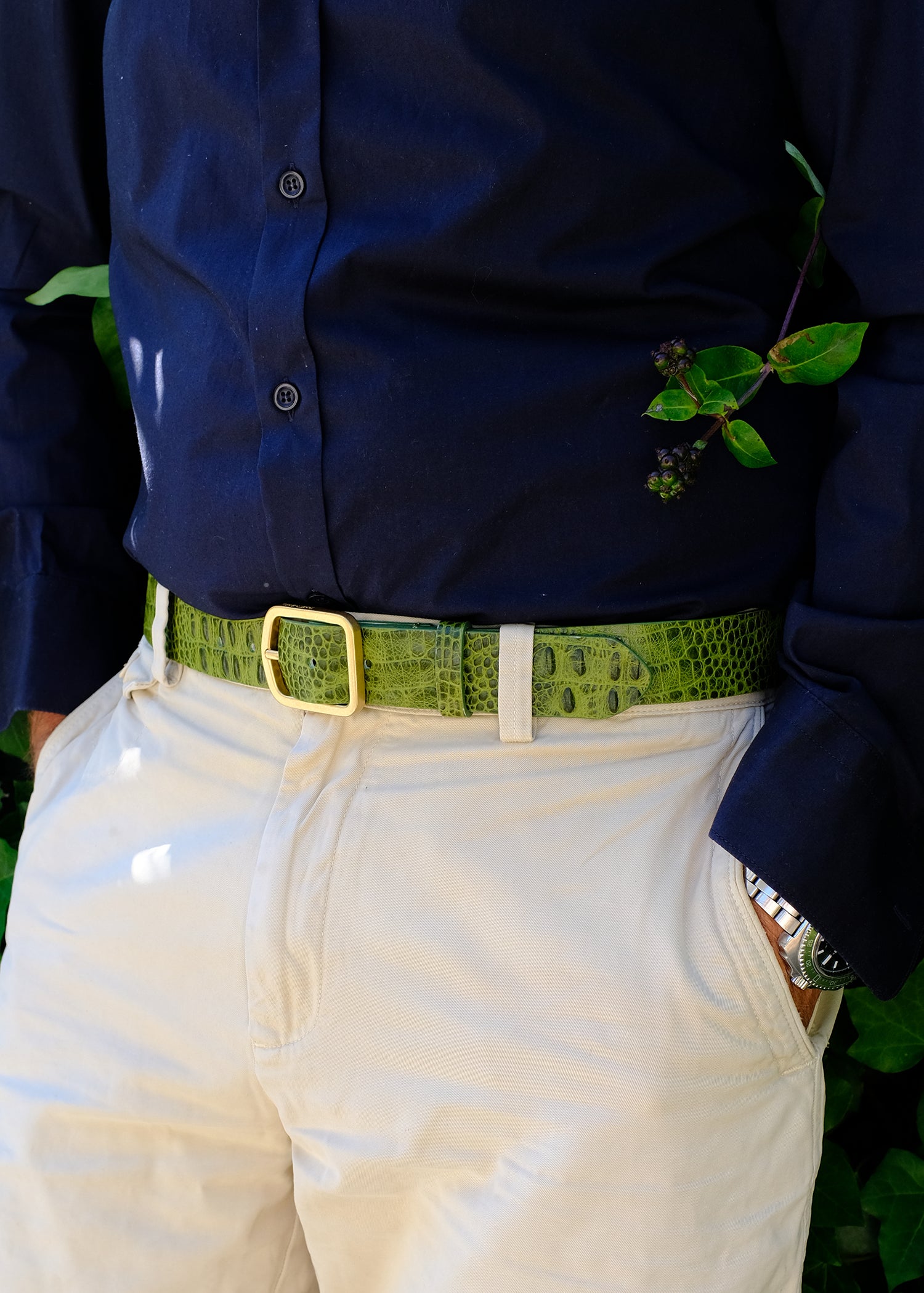 Close up on man wearing an atomic green croco embossed belt with a blue shirt and white trousers