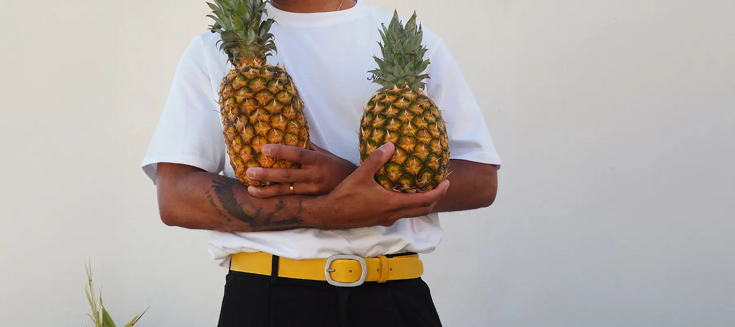 Close-up shot of a man´s waist with a classic smooth submarine yellow leather belt holding two pineapples.