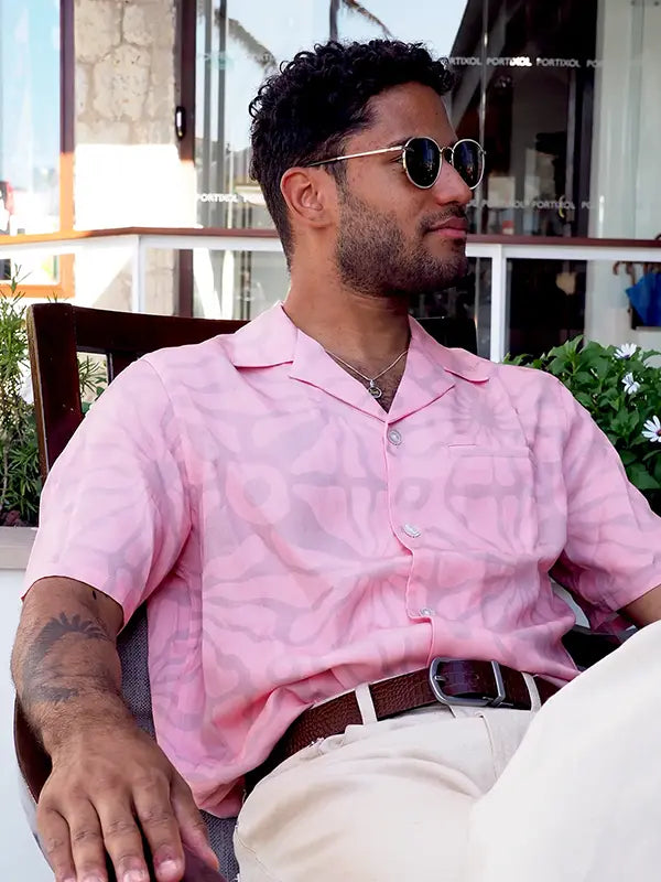 Lifestyle shot of man in sunglasses, white trousers with red classic leather belt with a silver buckle and a pink shirt.